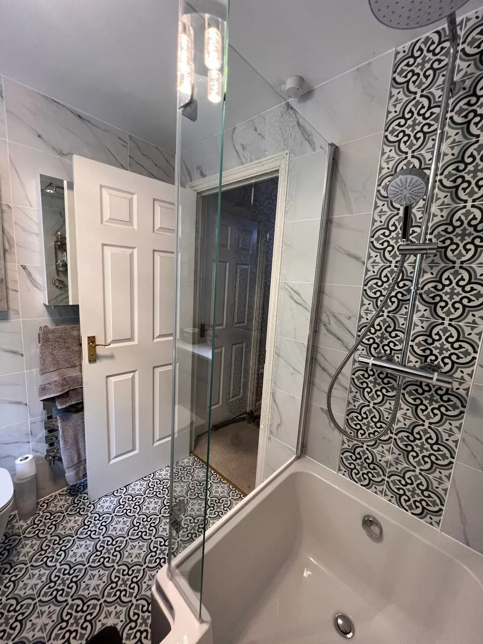 Bathroom with marble-effect walls, patterned floor and a decorative feature tile panel behind the shower bath, fitted by Basingstoke Bathrooms