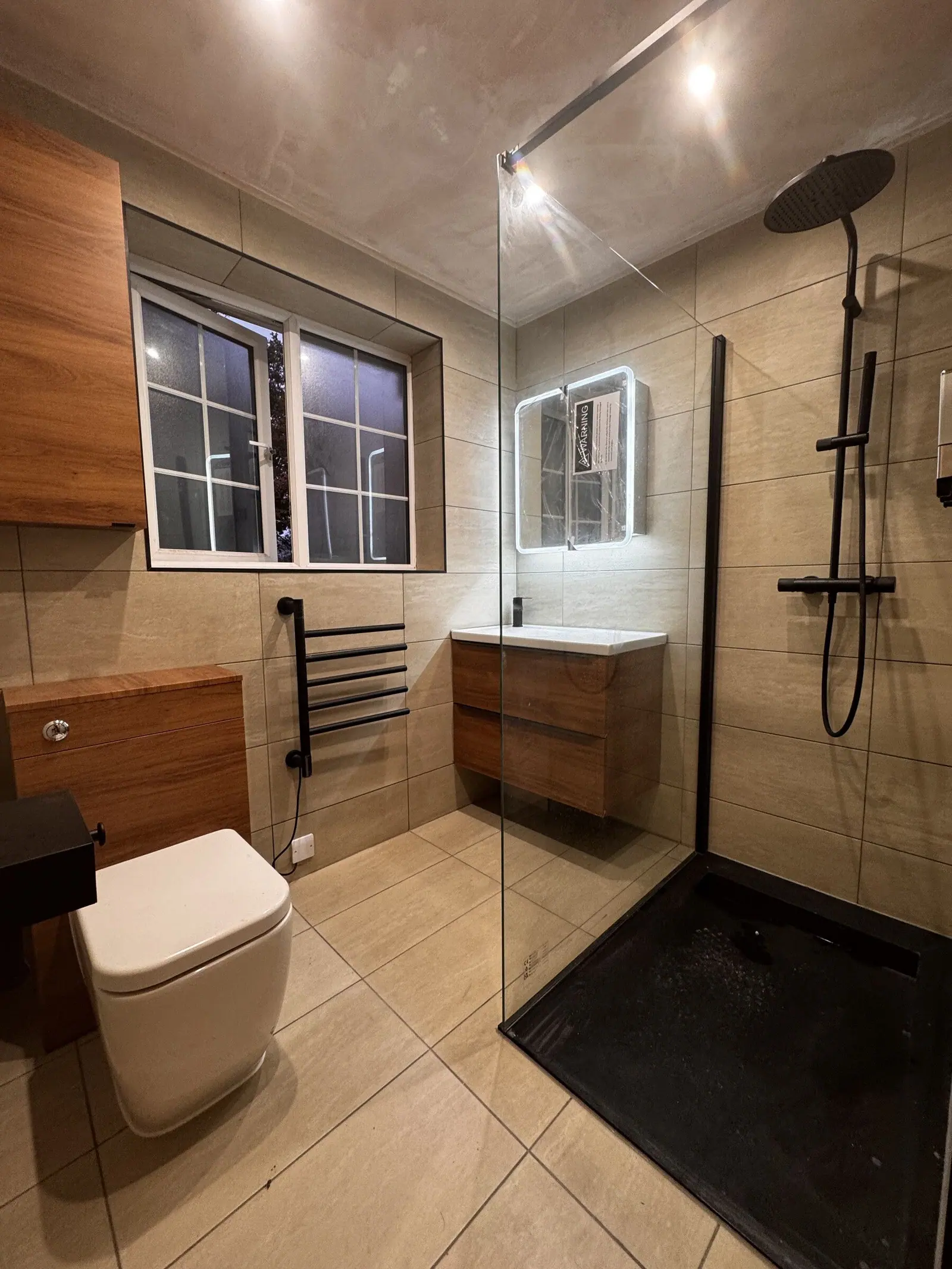 En-suite shower room with walnut vanity and WC unit, beige tiles and a black-framed walk-in shower screen, fitted by Basingstoke Bathrooms