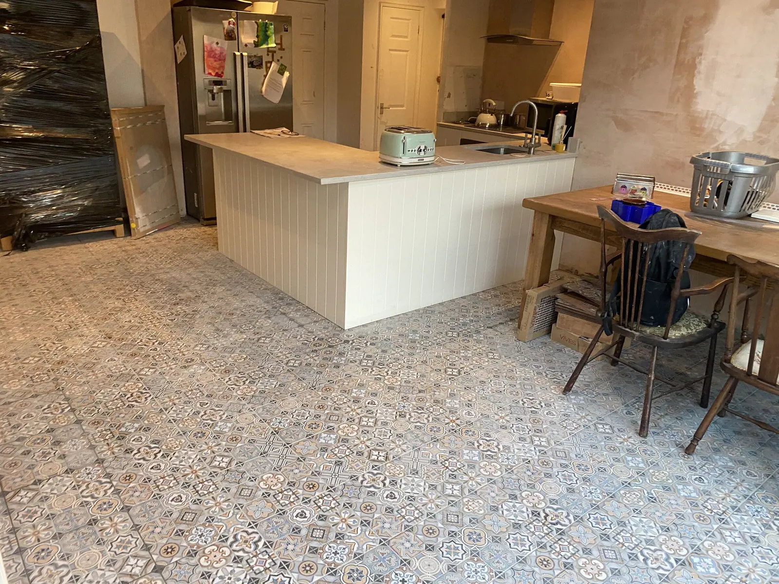 Kitchen part way through fitting: island and breakfast bar in place on a new patterned tiled floor, walls awaiting decoration, a Basingstoke Bathrooms job in progress